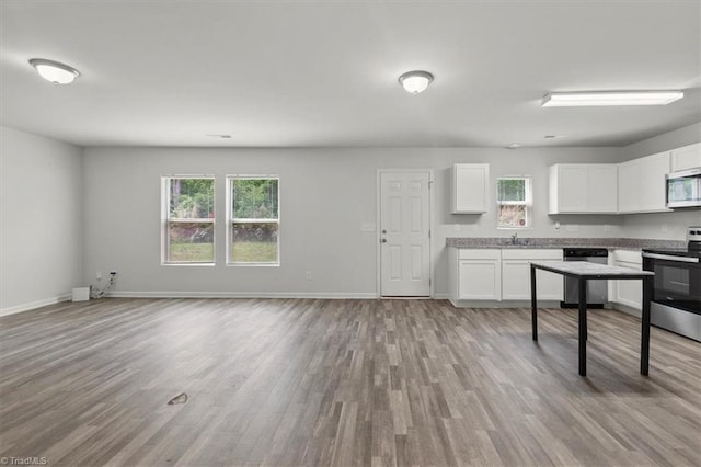 kitchen with white cabinetry, stainless steel appliances, baseboards, open floor plan, and light wood-type flooring