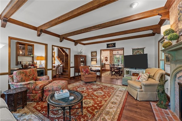 living area with beamed ceiling, a brick fireplace, stairway, and wood finished floors