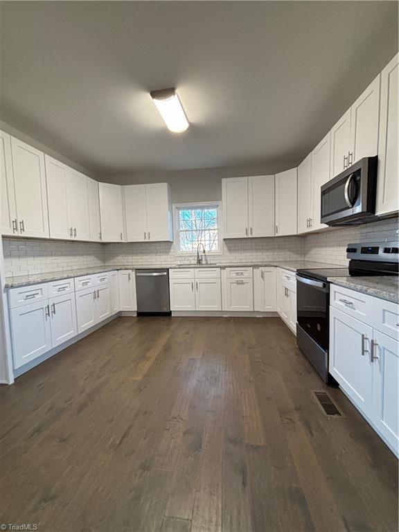 kitchen featuring light stone counters, dark hardwood / wood-style flooring, white cabinets, and appliances with stainless steel finishes