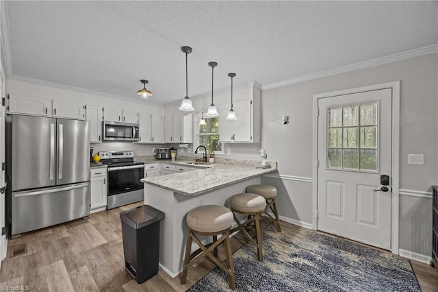 kitchen with appliances with stainless steel finishes, a peninsula, a textured ceiling, a sink, and white cabinets