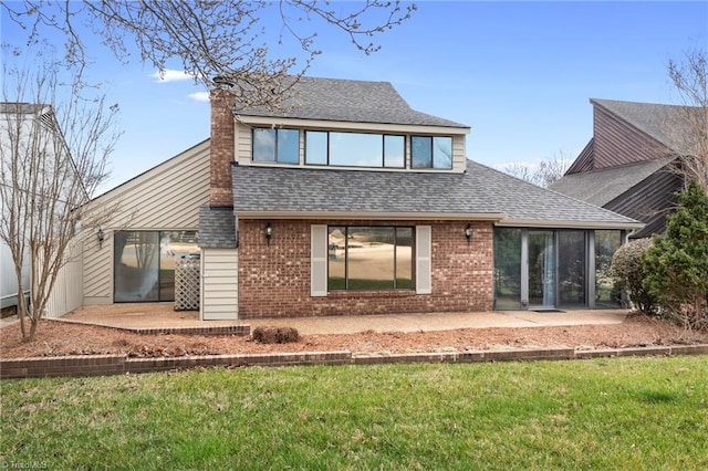 rear view of house featuring brick siding, a lawn, a shingled roof, and a patio