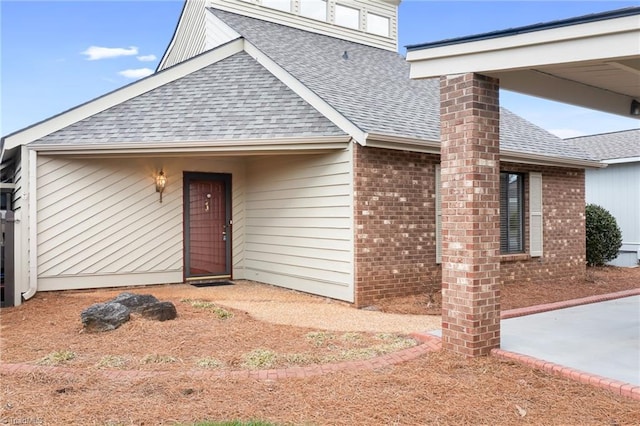 view of exterior entry with brick siding, roof with shingles, and a chimney