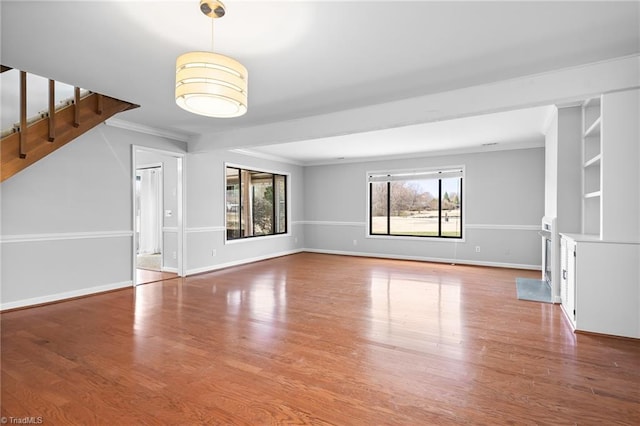 unfurnished living room featuring baseboards, wood finished floors, and ornamental molding