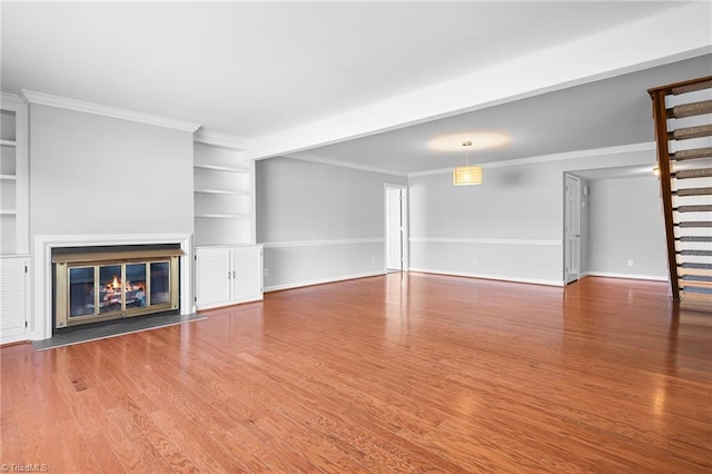 unfurnished living room featuring a glass covered fireplace, built in features, stairs, and wood finished floors