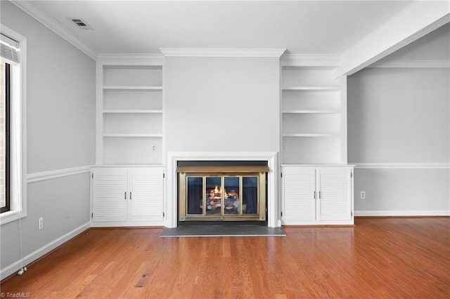 unfurnished living room featuring a glass covered fireplace, built in features, and wood finished floors