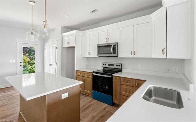 kitchen featuring a kitchen island, stainless steel appliances, pendant lighting, light wood-type flooring, and white cabinetry