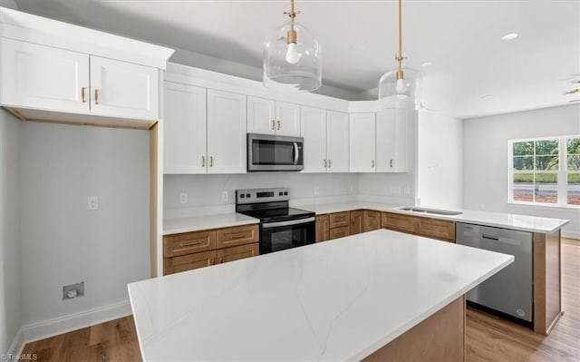 kitchen featuring kitchen peninsula, white cabinets, stainless steel appliances, decorative light fixtures, and a center island