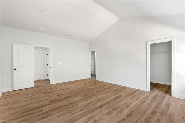 unfurnished bedroom featuring a spacious closet, high vaulted ceiling, a closet, and light hardwood / wood-style flooring