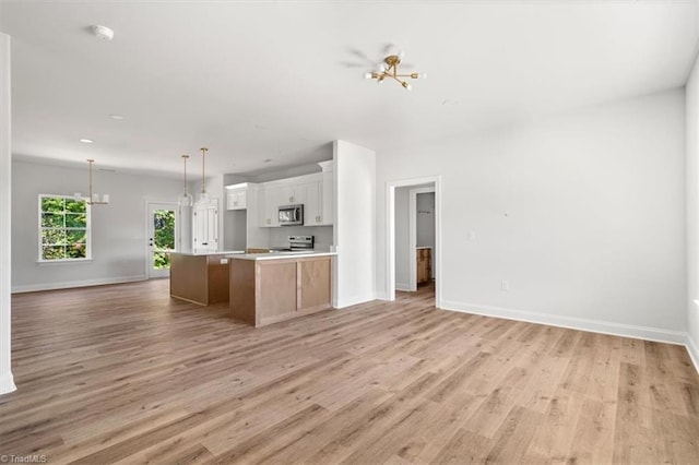 kitchen with light wood-type flooring, an island with sink, hanging light fixtures, white range oven, and white cabinets