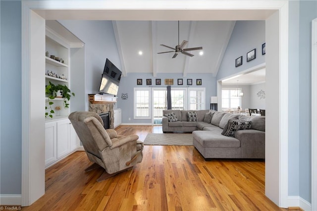 living room with beamed ceiling, a stone fireplace, light hardwood / wood-style flooring, and a wealth of natural light