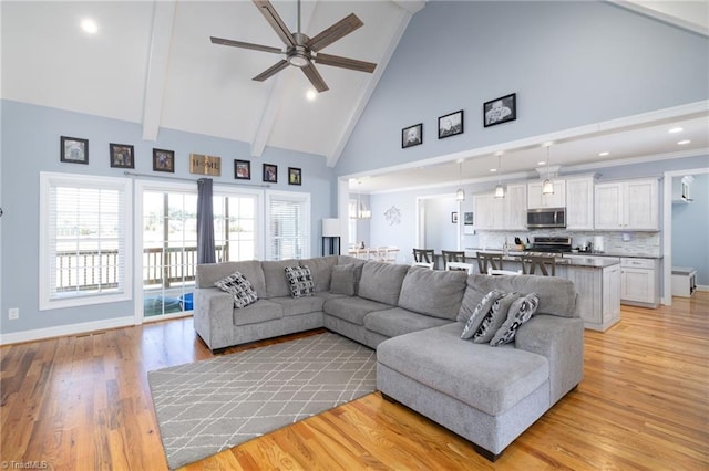 living room featuring high vaulted ceiling, beamed ceiling, light hardwood / wood-style floors, and ceiling fan