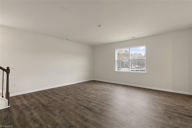 empty room with dark wood-style floors, baseboards, and stairs