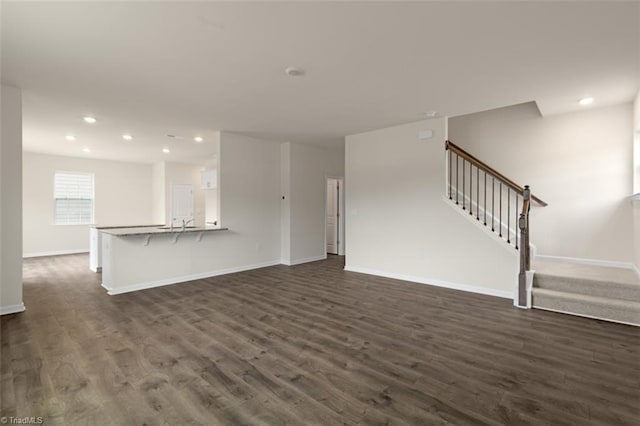 unfurnished living room with recessed lighting, dark wood-style flooring, baseboards, and stairs