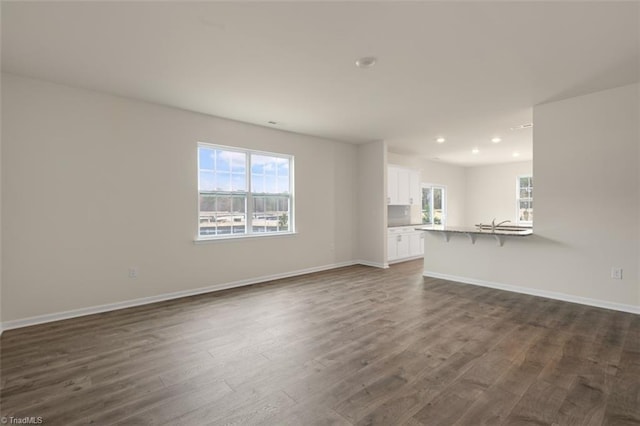 unfurnished living room with a healthy amount of sunlight, dark wood-style floors, and baseboards