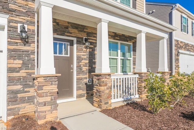 entrance to property featuring stone siding, covered porch, and a garage