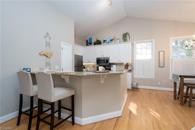 kitchen featuring lofted ceiling, stainless steel appliances, white cabinetry, light hardwood / wood-style flooring, and a kitchen breakfast bar