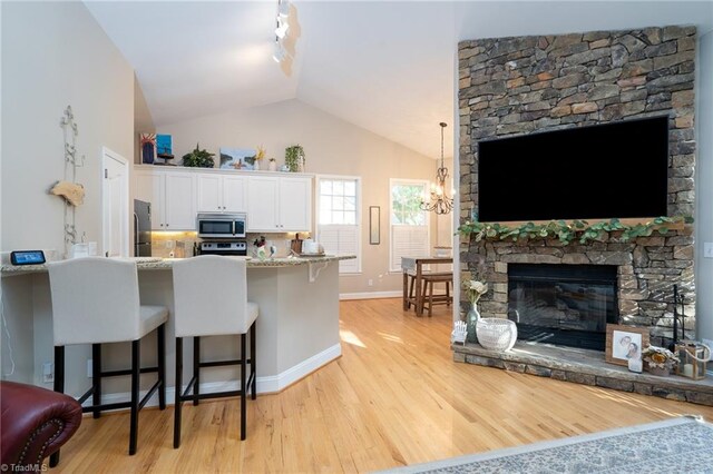 kitchen featuring light hardwood / wood-style floors, a breakfast bar area, vaulted ceiling, white cabinets, and appliances with stainless steel finishes