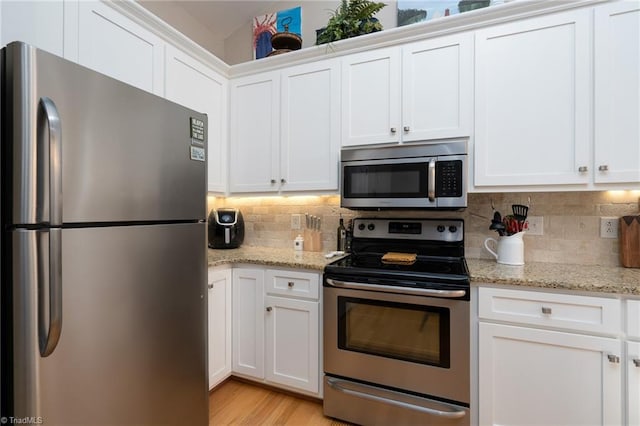 kitchen with white cabinets, stainless steel appliances, backsplash, and light stone countertops