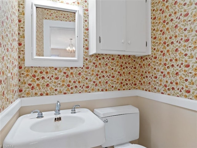 bathroom featuring toilet, sink, and an inviting chandelier