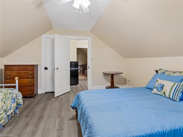 bedroom with ceiling fan, wood-type flooring, lofted ceiling, and black fridge