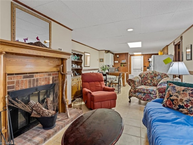 living room featuring ornamental molding, wooden walls, light tile patterned floors, and a brick fireplace