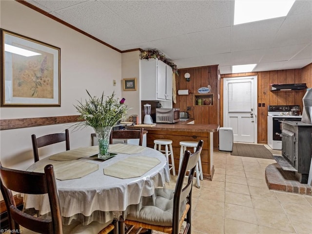 dining area featuring crown molding, light tile patterned flooring, and wood walls