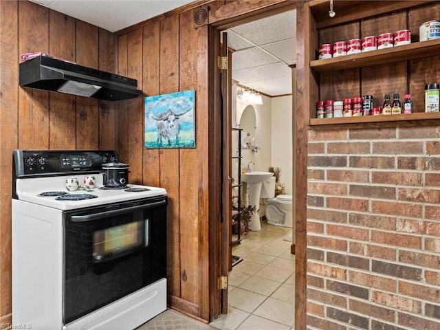 kitchen with white range with electric stovetop, wood walls, sink, and light tile patterned floors