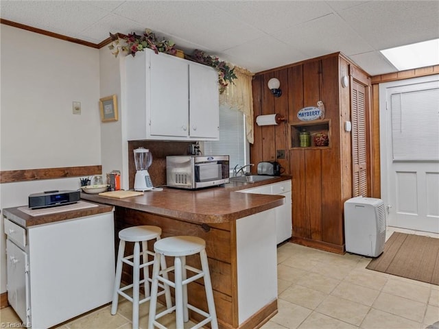 kitchen featuring kitchen peninsula, ornamental molding, sink, light tile patterned floors, and white cabinetry