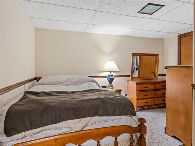 bedroom with a drop ceiling and light colored carpet