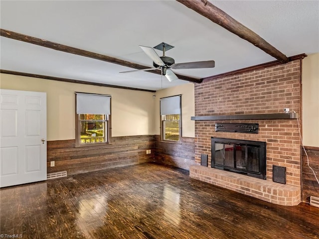 unfurnished living room with beam ceiling, ceiling fan, wood-type flooring, a brick fireplace, and wooden walls