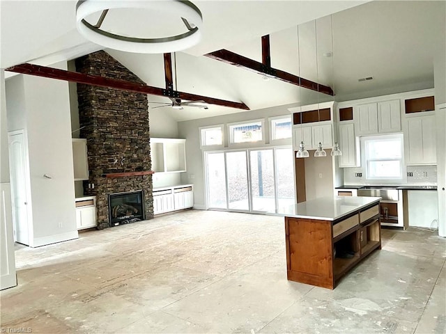 kitchen featuring a fireplace, ceiling fan, high vaulted ceiling, beamed ceiling, and a center island