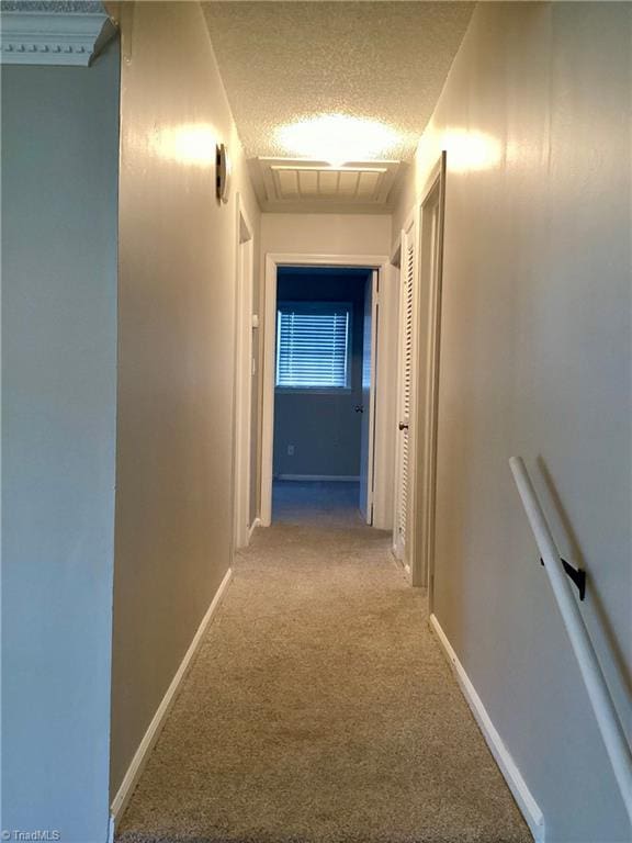 hallway featuring baseboards, visible vents, a textured ceiling, and carpet