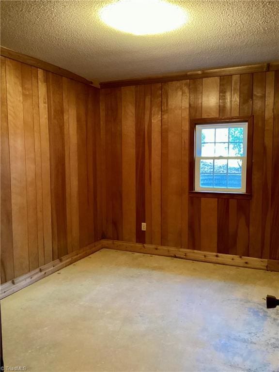 empty room featuring a textured ceiling, concrete flooring, and wood walls