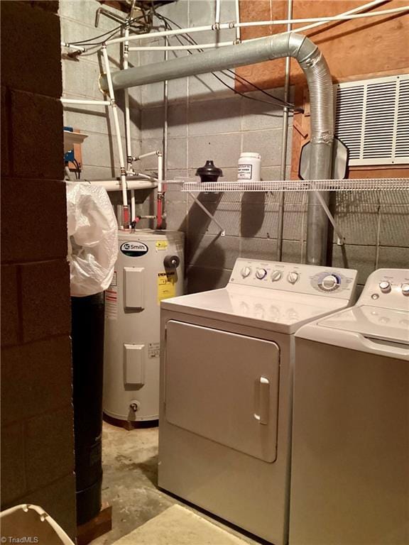 clothes washing area featuring water heater, laundry area, washer and dryer, and concrete block wall