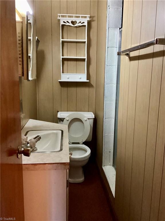 bathroom featuring a shower stall, toilet, vanity, and wood walls