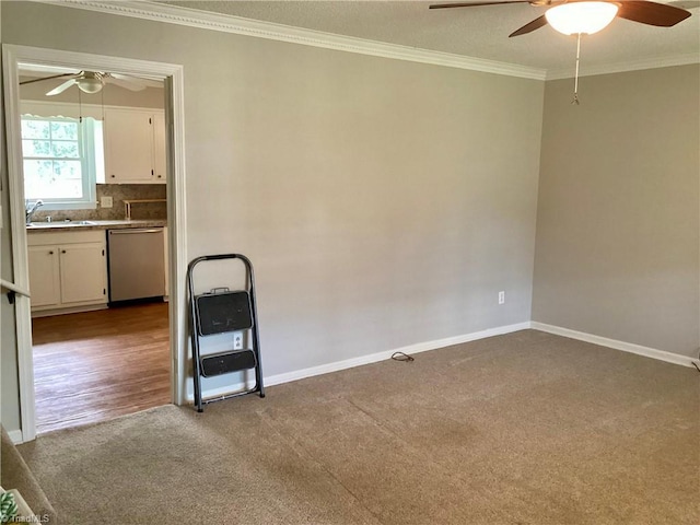 carpeted empty room with ceiling fan, crown molding, baseboards, and a sink