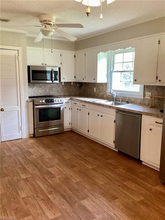 kitchen with wood finished floors, white cabinetry, stainless steel appliances, and a sink