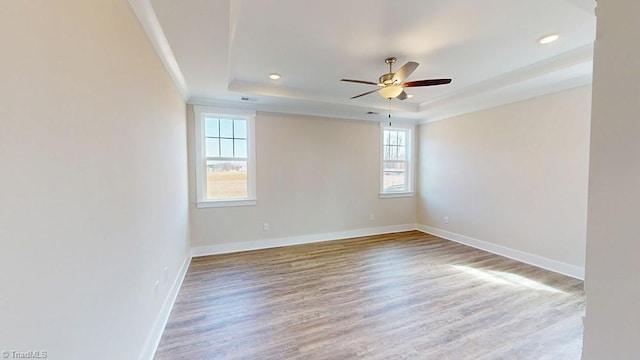 empty room with a raised ceiling, wood finished floors, recessed lighting, baseboards, and ceiling fan