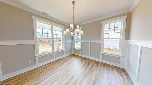 unfurnished dining area with visible vents, crown molding, wood finished floors, a notable chandelier, and a decorative wall