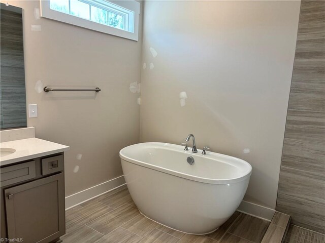 bathroom featuring wood finish floors, baseboards, a freestanding bath, and vanity