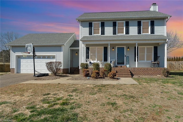 traditional-style home with covered porch, a garage, driveway, a chimney, and a front yard