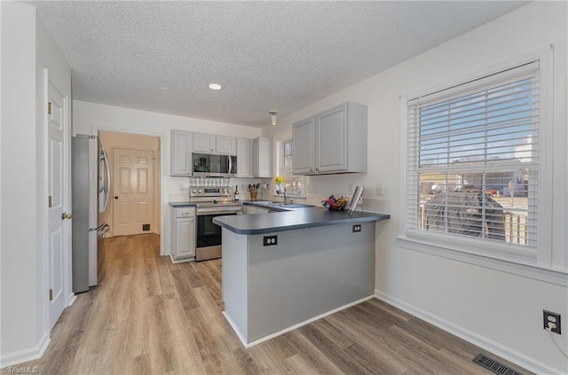 kitchen with visible vents, dark countertops, appliances with stainless steel finishes, a peninsula, and gray cabinetry