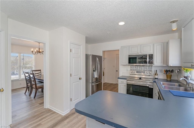 kitchen with stainless steel appliances, a sink, light wood-style floors, hanging light fixtures, and an inviting chandelier