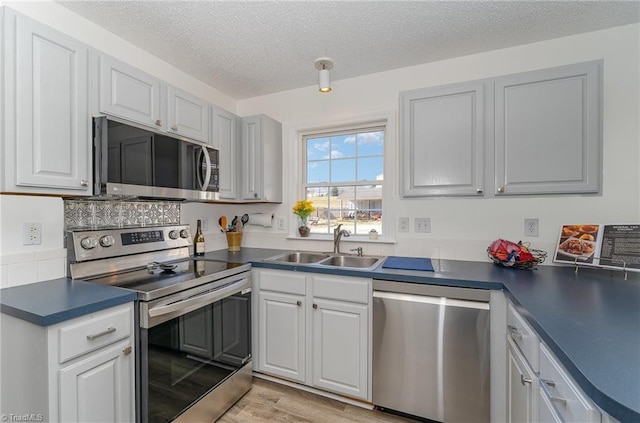 kitchen featuring a textured ceiling, light wood-style flooring, stainless steel appliances, a sink, and dark countertops