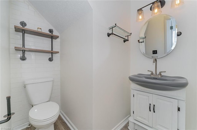 half bath with toilet, vaulted ceiling, a textured ceiling, vanity, and baseboards