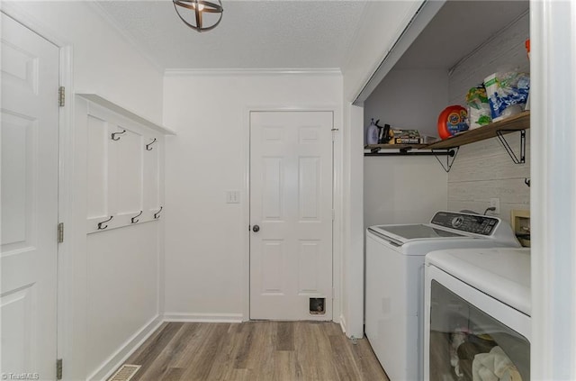 laundry area featuring crown molding, light wood-style flooring, a textured ceiling, washer and dryer, and laundry area