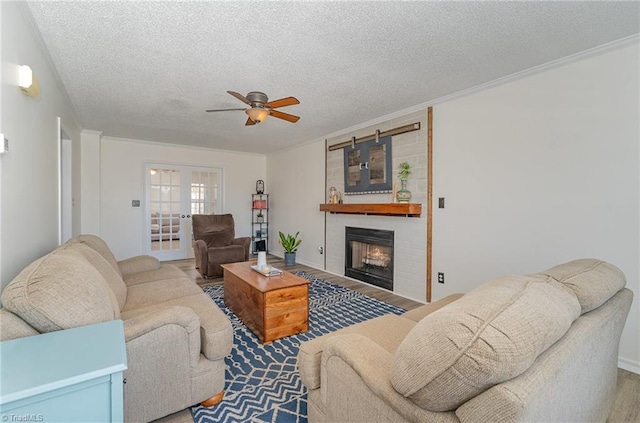 living room with a large fireplace, ceiling fan, ornamental molding, and a textured ceiling