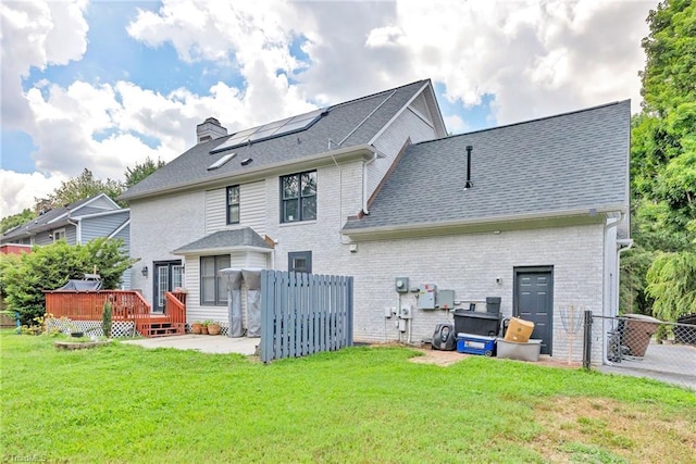 back of property with a wooden deck, a yard, and solar panels