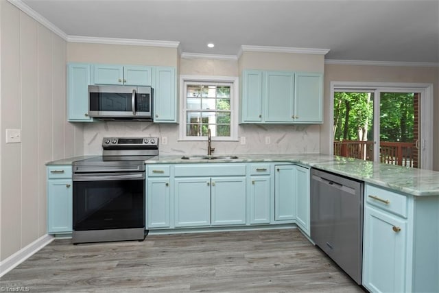 kitchen with appliances with stainless steel finishes, a sink, a peninsula, light wood-type flooring, and ornamental molding