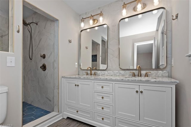 full bathroom with a tile shower, double vanity, tasteful backsplash, toilet, and wood finished floors